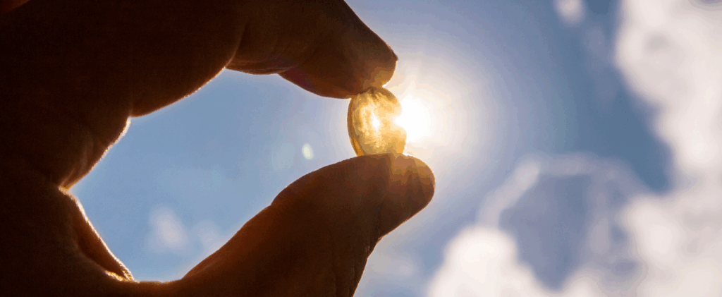 Hand holding a Vitamin D pill towards the sun
