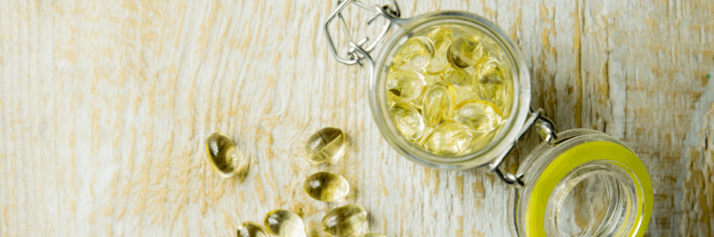 Vitamin D pills in a glass jar with some scattered on a wooden table.
