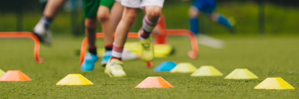Children running through cones during an outdoor youth sports practice.